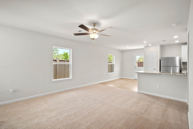 unfurnished living room with light carpet, ceiling fan, and a healthy amount of sunlight