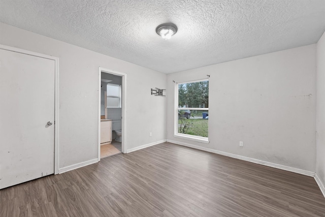 unfurnished bedroom featuring hardwood / wood-style floors, a textured ceiling, and ensuite bath