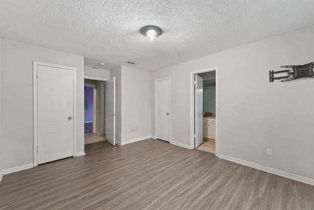 unfurnished bedroom featuring hardwood / wood-style floors, a textured ceiling, and connected bathroom