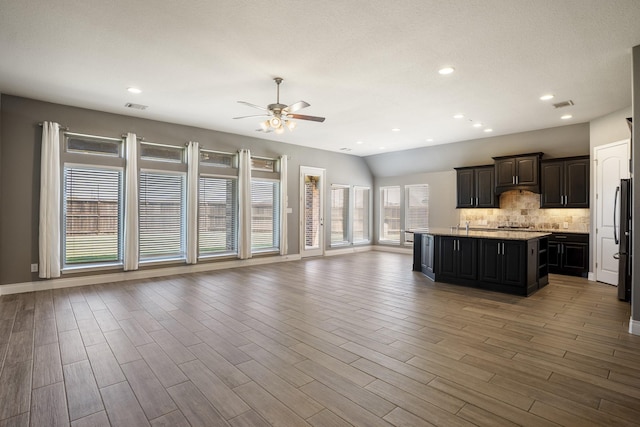 kitchen with dark brown cabinetry, ceiling fan, backsplash, vaulted ceiling, and a center island with sink