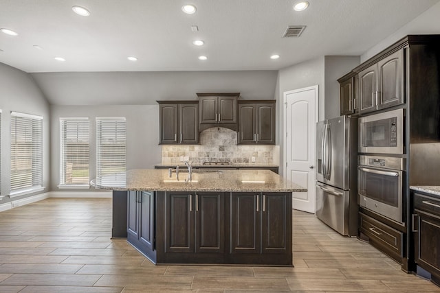 kitchen with a center island with sink, dark brown cabinets, and appliances with stainless steel finishes