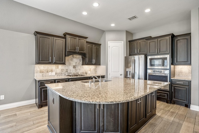 kitchen with dark brown cabinets, a kitchen island with sink, sink, and appliances with stainless steel finishes