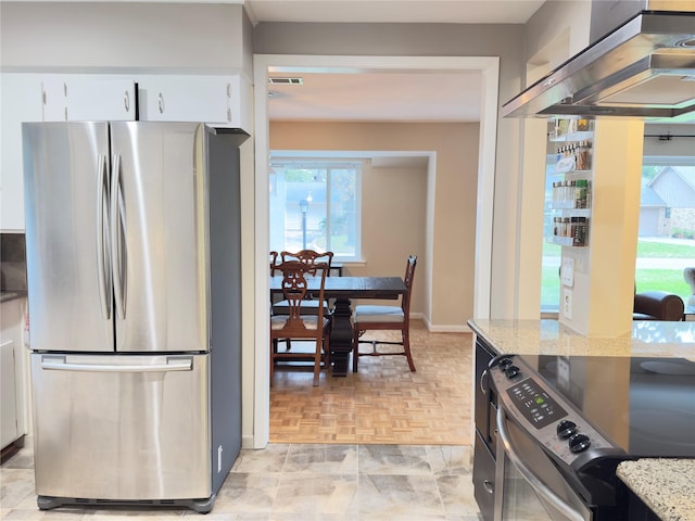 kitchen with appliances with stainless steel finishes, wall chimney exhaust hood, white cabinetry, and light stone counters