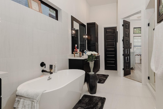 bathroom with tile patterned flooring, vanity, a bath, and tile walls