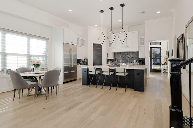 kitchen featuring decorative backsplash, light wood-type flooring, decorative light fixtures, a center island with sink, and built in fridge