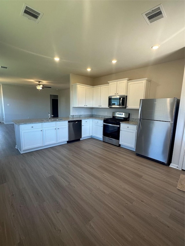 kitchen featuring kitchen peninsula, appliances with stainless steel finishes, white cabinetry, and dark wood-type flooring