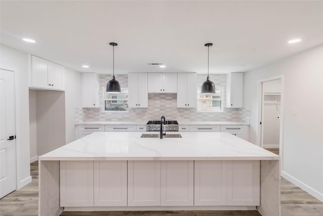 kitchen with white cabinetry, light stone countertops, an island with sink, and hanging light fixtures