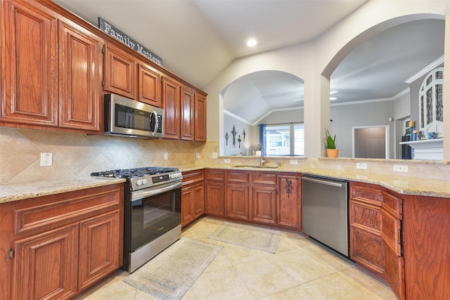 kitchen with sink, vaulted ceiling, decorative backsplash, appliances with stainless steel finishes, and light stone counters