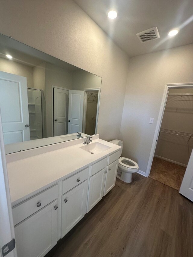 bathroom with hardwood / wood-style flooring, vanity, toilet, and a shower with door