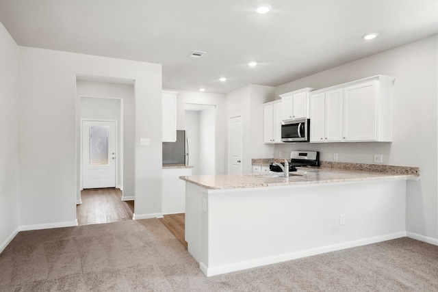 kitchen featuring white cabinetry, light stone counters, kitchen peninsula, light carpet, and appliances with stainless steel finishes