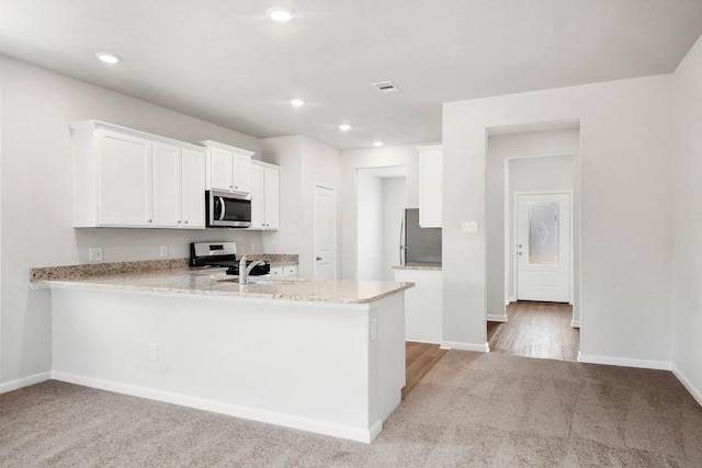 kitchen with light stone countertops, white cabinetry, kitchen peninsula, light carpet, and appliances with stainless steel finishes