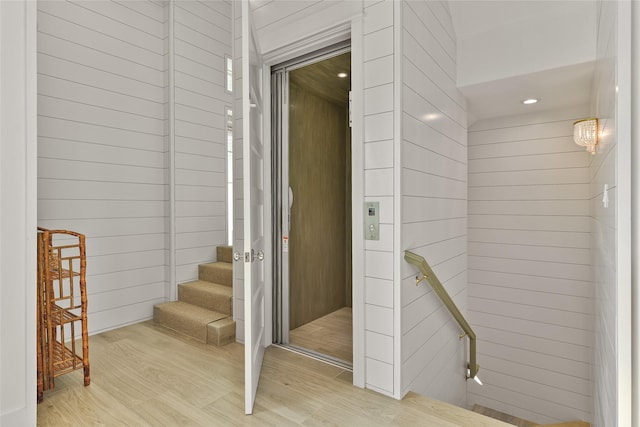 stairway with wood-type flooring, wood walls, and elevator