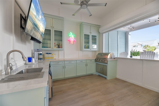 kitchen with ceiling fan, sink, green cabinets, light hardwood / wood-style flooring, and light stone countertops