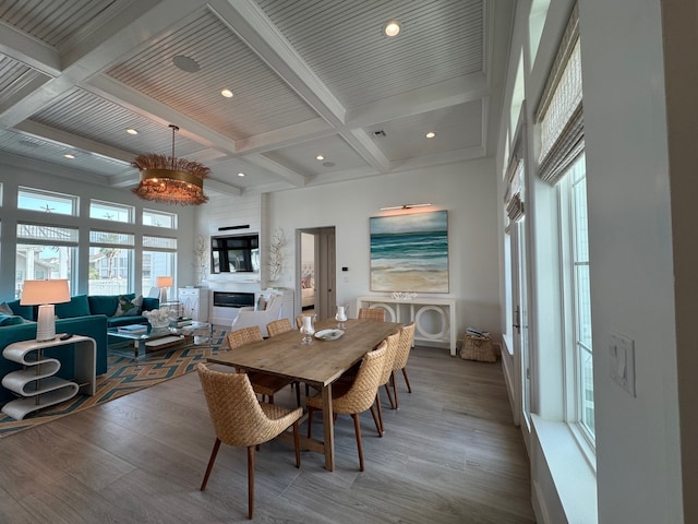 dining area with hardwood / wood-style floors, beamed ceiling, a fireplace, a chandelier, and coffered ceiling