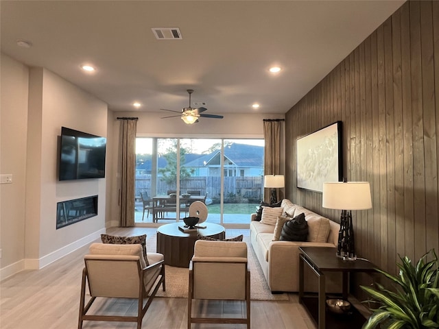 living room with wooden walls, ceiling fan, and light wood-type flooring