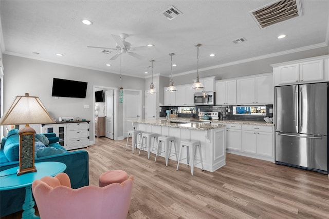 kitchen with ceiling fan, pendant lighting, a center island with sink, white cabinets, and appliances with stainless steel finishes