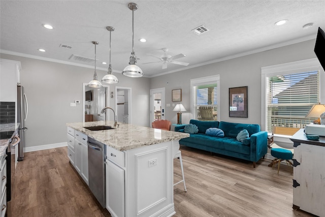 kitchen featuring hanging light fixtures, white cabinetry, a kitchen island with sink, and sink