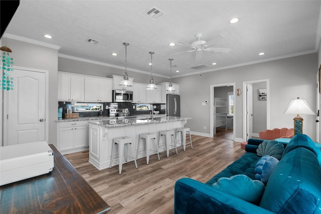 kitchen featuring appliances with stainless steel finishes, ceiling fan, a center island with sink, white cabinetry, and hanging light fixtures