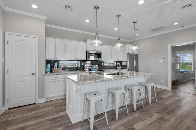 kitchen featuring decorative backsplash, appliances with stainless steel finishes, a kitchen island with sink, hardwood / wood-style floors, and white cabinetry