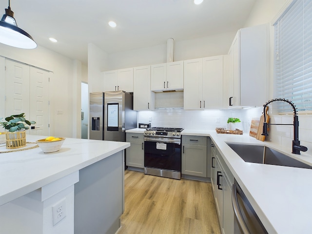 kitchen with appliances with stainless steel finishes, tasteful backsplash, sink, decorative light fixtures, and light hardwood / wood-style flooring