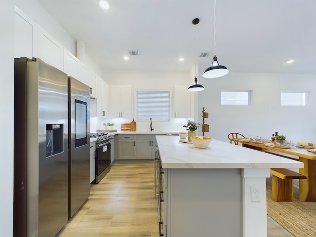 kitchen with pendant lighting, light hardwood / wood-style flooring, appliances with stainless steel finishes, a kitchen island, and white cabinetry