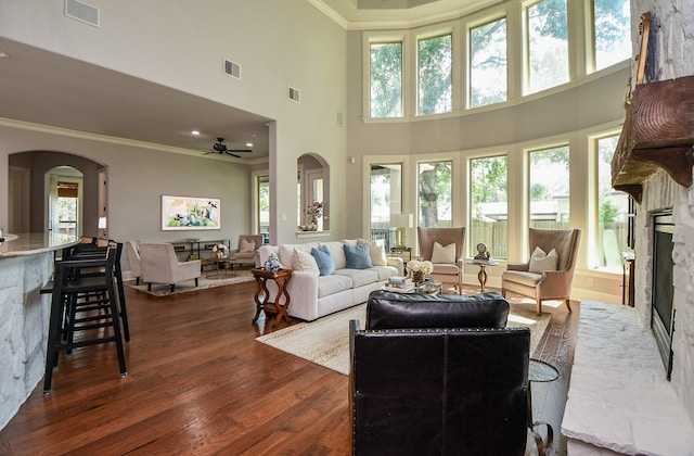 living room with ornamental molding, dark hardwood / wood-style floors, a towering ceiling, ceiling fan, and a fireplace