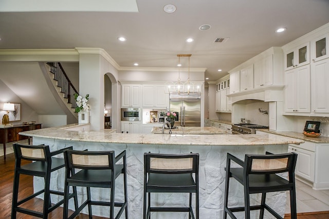 kitchen featuring decorative light fixtures, a breakfast bar area, white cabinets, built in appliances, and light stone counters