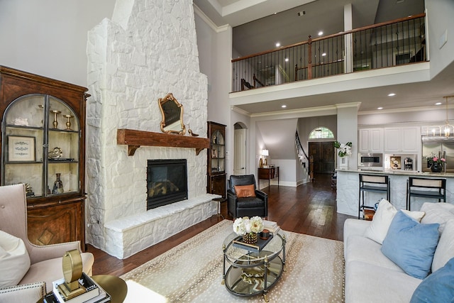 living room featuring dark wood-type flooring, a towering ceiling, ornamental molding, and a fireplace