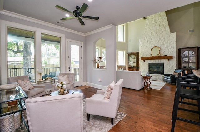 living room with ornamental molding, a stone fireplace, dark wood-type flooring, and ceiling fan