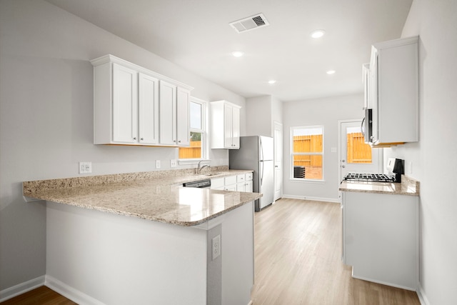 kitchen with white cabinets, light stone countertops, light wood-type flooring, kitchen peninsula, and stainless steel appliances