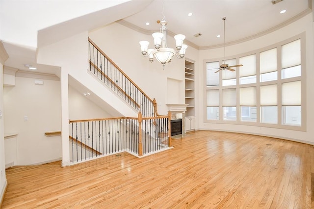 unfurnished living room featuring built in shelves, light hardwood / wood-style flooring, ceiling fan with notable chandelier, and ornamental molding