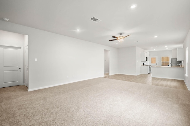 unfurnished living room featuring ceiling fan, sink, and light carpet