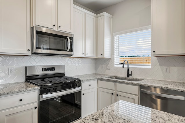 kitchen with light stone countertops, appliances with stainless steel finishes, backsplash, sink, and white cabinets