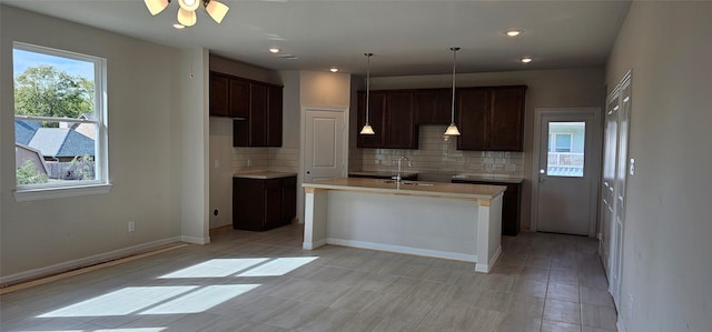 kitchen with sink, tasteful backsplash, a healthy amount of sunlight, and an island with sink