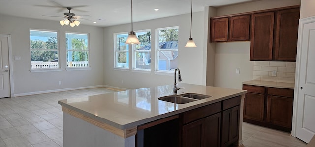 kitchen featuring ceiling fan, sink, backsplash, pendant lighting, and a kitchen island with sink