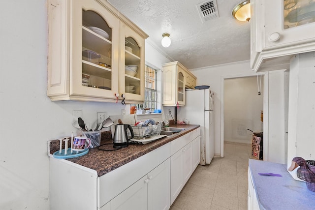 kitchen featuring white refrigerator, sink, ornamental molding, and a textured ceiling