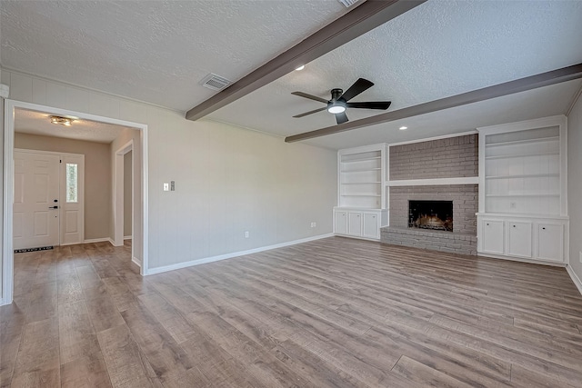 unfurnished living room with a brick fireplace, built in shelves, a textured ceiling, ceiling fan, and beamed ceiling