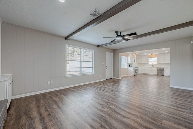 unfurnished living room featuring beam ceiling, wood-type flooring, a textured ceiling, wooden walls, and ceiling fan with notable chandelier