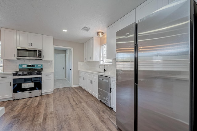 kitchen featuring white cabinets, sink, a textured ceiling, appliances with stainless steel finishes, and light hardwood / wood-style floors