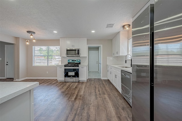 kitchen with appliances with stainless steel finishes, tasteful backsplash, sink, white cabinets, and hardwood / wood-style floors