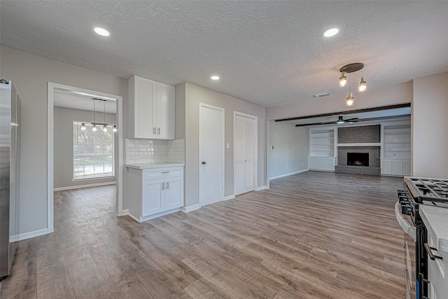 kitchen featuring ceiling fan, a brick fireplace, stainless steel gas range, backsplash, and white cabinets