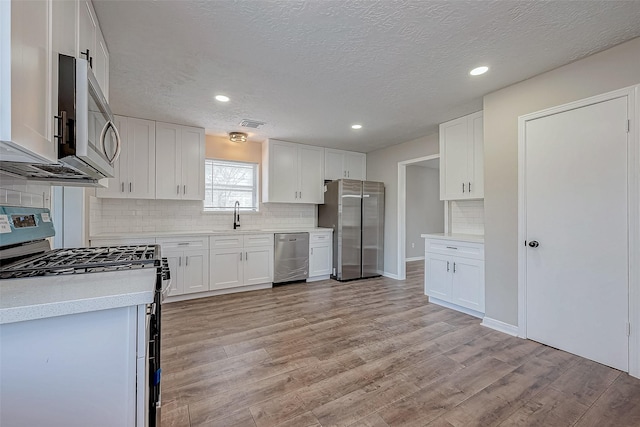 kitchen with sink, a textured ceiling, appliances with stainless steel finishes, tasteful backsplash, and white cabinetry