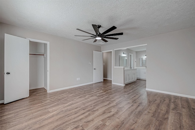 unfurnished bedroom with ensuite bathroom, a textured ceiling, ceiling fan, light hardwood / wood-style flooring, and a closet