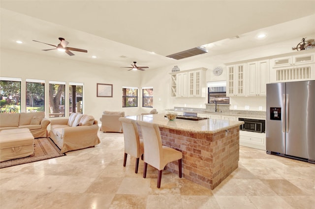 kitchen with black microwave, a center island, light stone countertops, a kitchen breakfast bar, and stainless steel fridge with ice dispenser