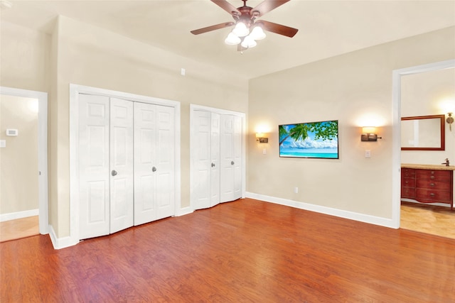 unfurnished bedroom featuring wood-type flooring, two closets, ceiling fan, and ensuite bathroom