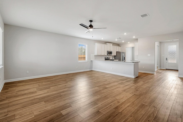 unfurnished living room with ceiling fan, light wood-type flooring, and sink