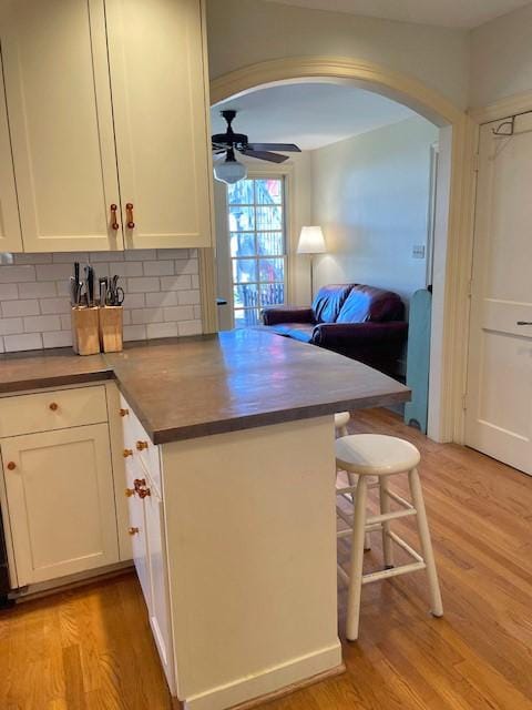 kitchen with kitchen peninsula, light wood-type flooring, tasteful backsplash, ceiling fan, and white cabinetry