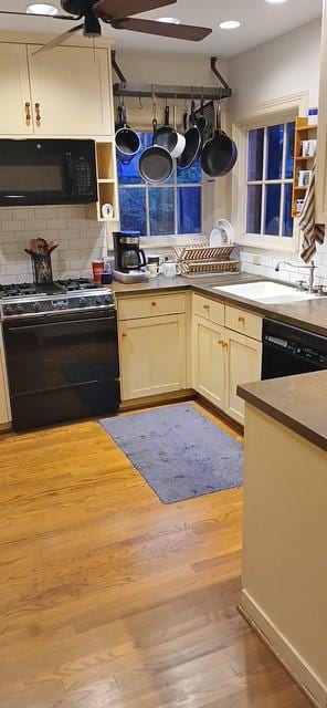 kitchen featuring sink, backsplash, cream cabinetry, black appliances, and light wood-type flooring