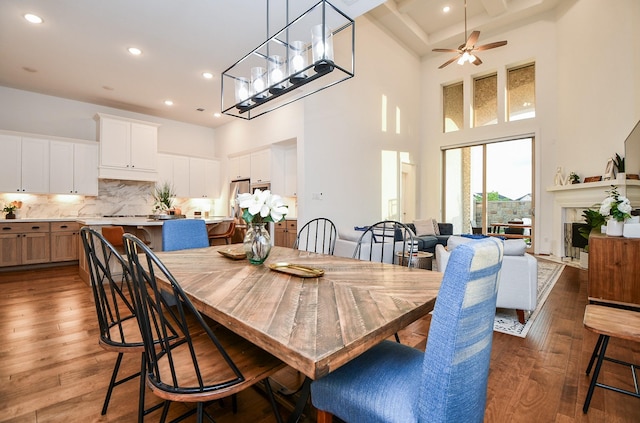 dining area featuring ceiling fan, coffered ceiling, wood-type flooring, and a high ceiling