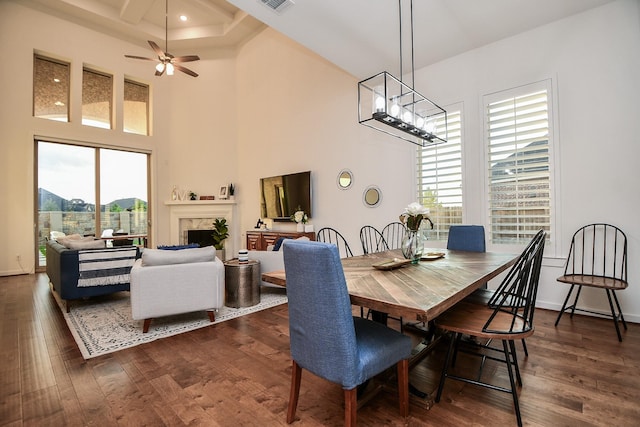 dining room featuring a towering ceiling, dark wood-type flooring, and ceiling fan with notable chandelier